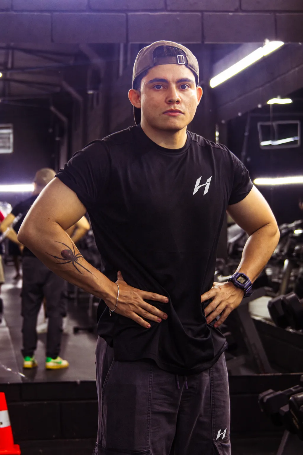 Atleta Hustform con camiseta negra y manos en la cintura, tatuaje visible en el antebrazo